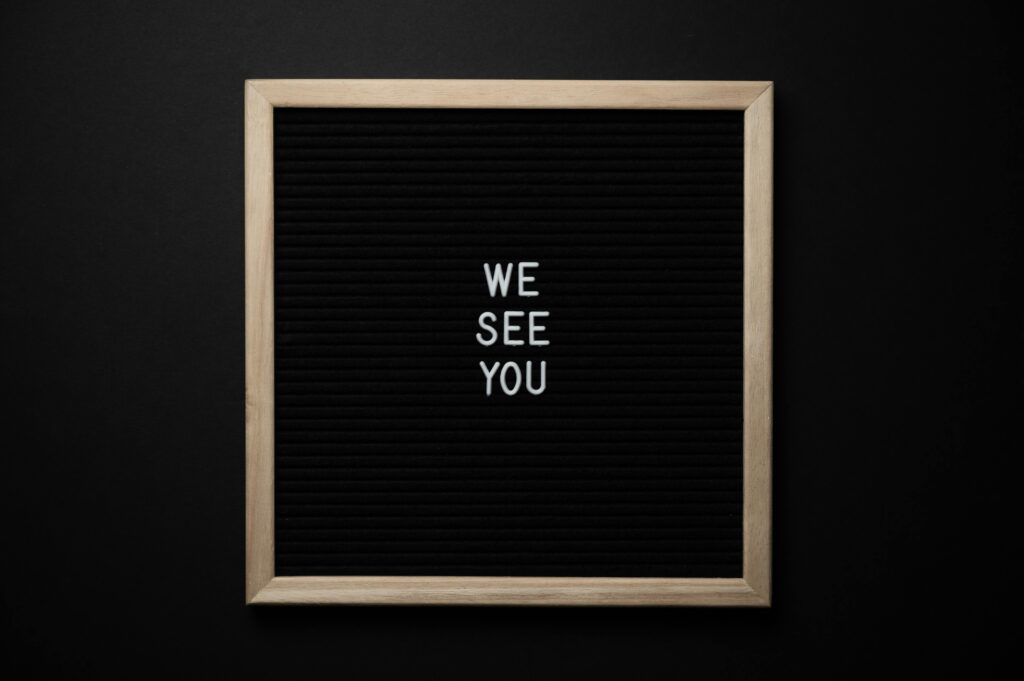 Black letter board with the message 'We See You' on a dark background, conveying a theme of awareness.
